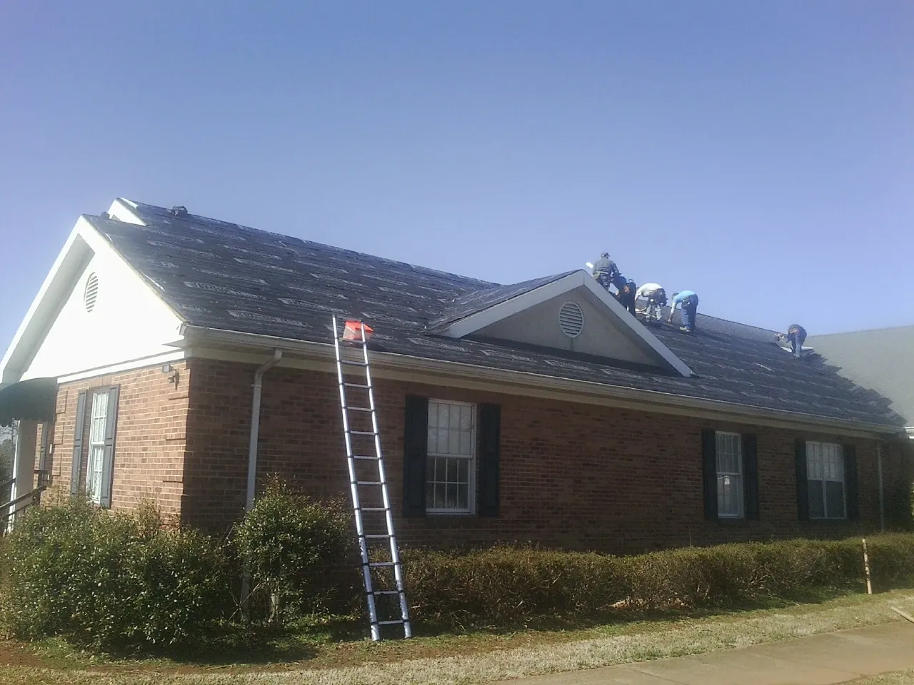 Crew tearing shingles off a brick ranch roof with a ladder set — Metal Roof Repair work by our crew in Landisville