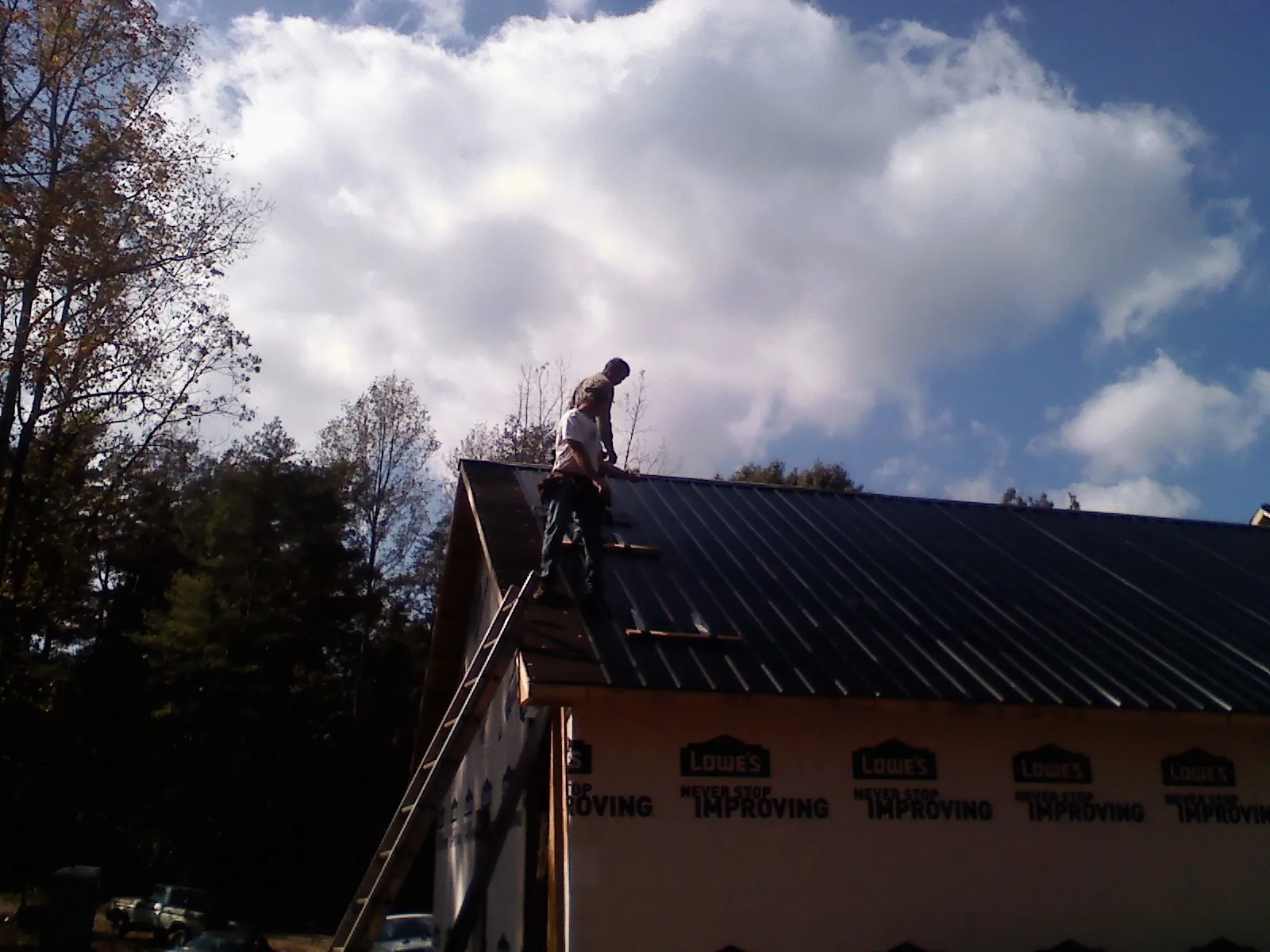 Roofer fastening dark metal panels high against a cloudy sky, from a Roof Inspection job in Landisville